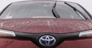 Front view of a red Toyota with rain droplets on the hood and logo.