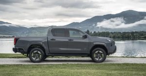 Side view of a gray Toyota Hilux BEV near a lake, showcasing large wheels and a rugged design.