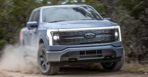 Front angle of Ford F-150 Lightning, showcasing headlights, grille, and rugged terrain.