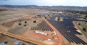 Aerial view of a large solar farm with rows of solar panels and sparse vegetation.
