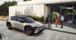 Silver electric vehicle parked at a charging station outside a modern building.