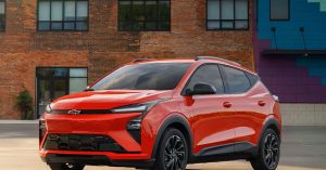 Red Chevy Bolt EV parked in an urban setting, showcasing a sleek front design and black wheels.