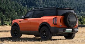 Orange Ford Bronco EV, rear angle, large spare tire, rugged wheels, natural setting.