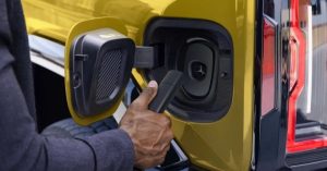 A person connects a charging cable to the rear charging port of a yellow vehicle.