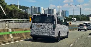 The Kia PV7 Electric Van is camouflaged, seen from the rear on a road.