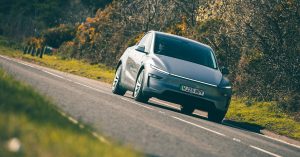 Silver electric vehicle driving on a road, featuring sleek design and modern wheels.