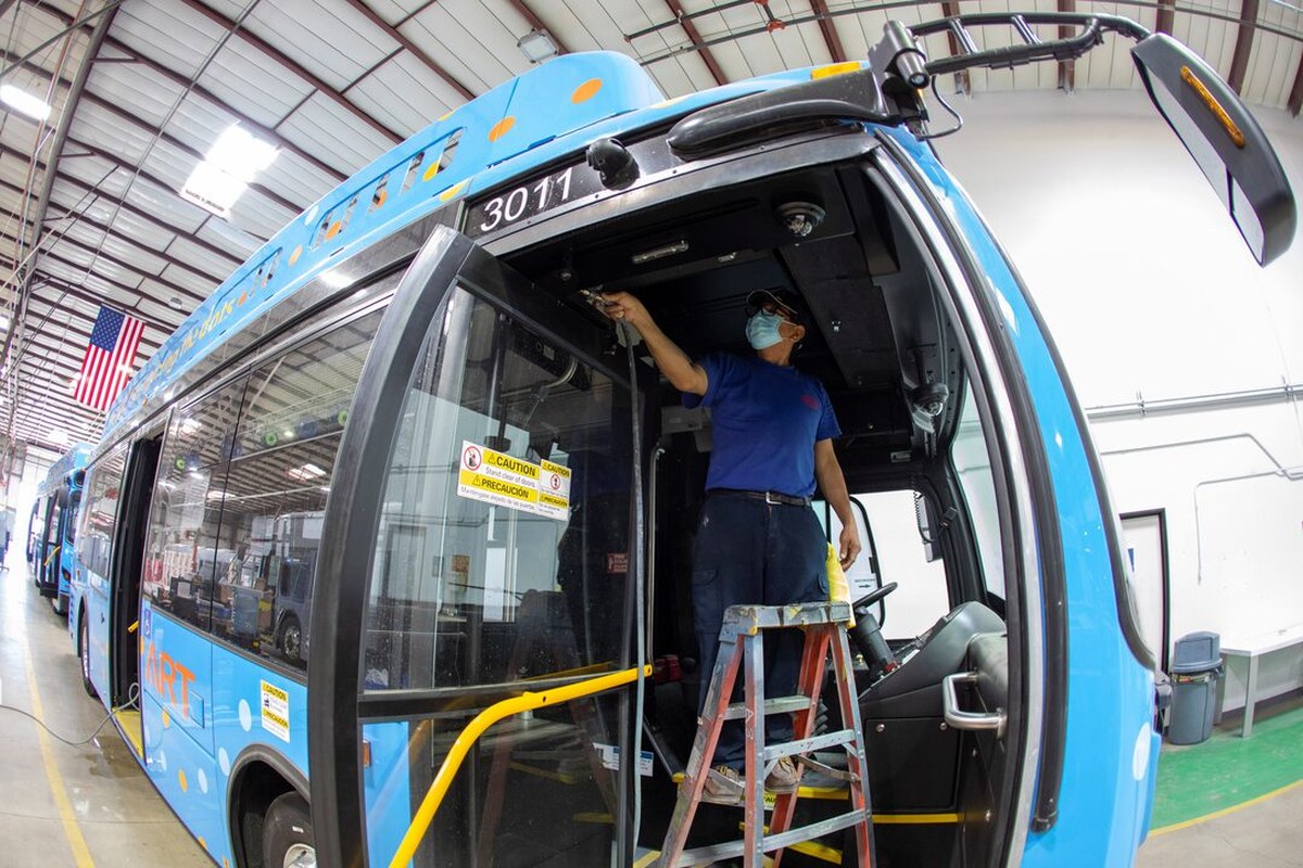 Interior view of a BYD electric bus with a worker on a ladder, dashboard visible.
