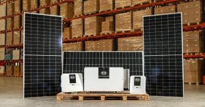 The image shows solar panels and inverters displayed in a warehouse setting.