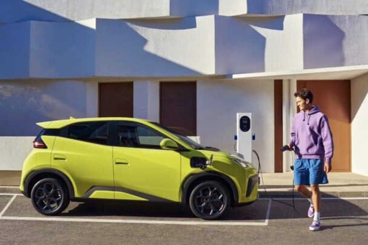 A bright green EV parked beside a charging station, with a man holding a charging cable.