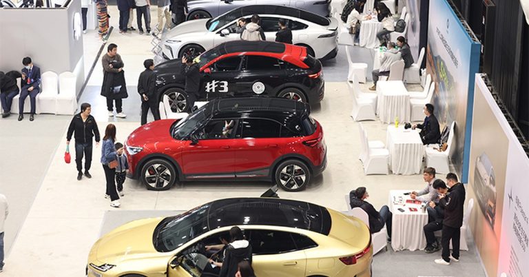 Aerial view of multiple electric vehicles in a showroom, featuring red, black, and gold models.