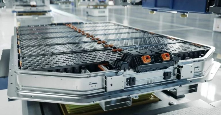 Image shows a solid-state battery pack in a factory setting, featuring multiple battery cells and connectors.