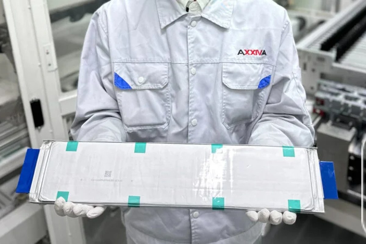 A person in a lab coat holds a solid-state battery in a factory setting.