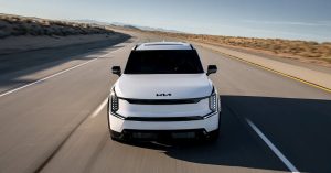 Front view of a white Kia SUV on a highway, showcasing sleek headlights and a modern grille.