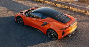 The Lotus Emira 420 Sport is shown from a high angle, highlighting its orange exterior, black roof, and sporty wheels.