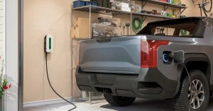 Gray electric vehicle parked in a garage, charging port connected, shelves in background.