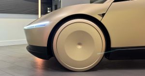 The image shows a side view of a Tesla Cybercab with unique, large wheels and sleek design.