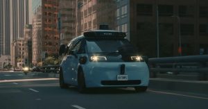 The vehicle is a Waymo robotaxi, shown from the front on a city road.