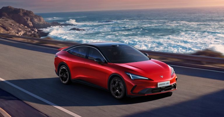 Red Arcfox Alpha S5 driving along a coastal road, showcasing sleek design and sporty wheels.