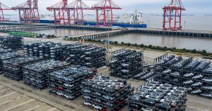 Aerial view of stacked vehicles in a shipping yard near a harbor.