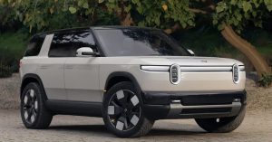 The image shows a Rivian SUV from a front-side angle, featuring large wheels and distinctive headlights.
